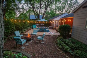 A backyard with a fire pit, outdoor furniture, and string lights.