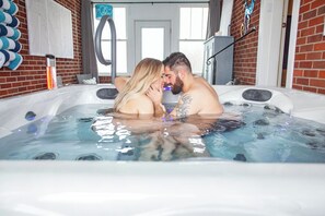 A couple in a hot tub with a brick wall and a door in the background.