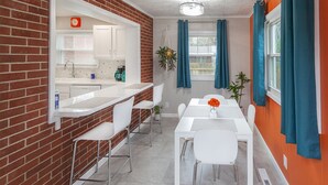 Una cocina moderna con armarios blancos, una pared de ladrillo decorativa y un comedor con una mesa y sillas blancas.