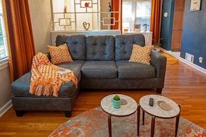 Un salon moderne avec un canapé d’angle, deux tables d’appoint et un meuble mural décoratif.