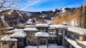 Una casa moderna de varios pisos con tejado nevado y vistas a un paisaje montañoso.