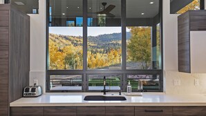 Una cocina moderna con un amplio ventanal que ofrece vistas a un páramo boscoso.