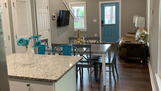 A modern kitchen with granite countertops, a dining area with blue chairs, and a living room with a sofa and a TV. - Ample Space in Grant Park, Close to Everything! (Atlanta)