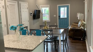 A modern kitchen with granite countertops, a dining area with blue chairs, and a living room with a sofa and a TV.