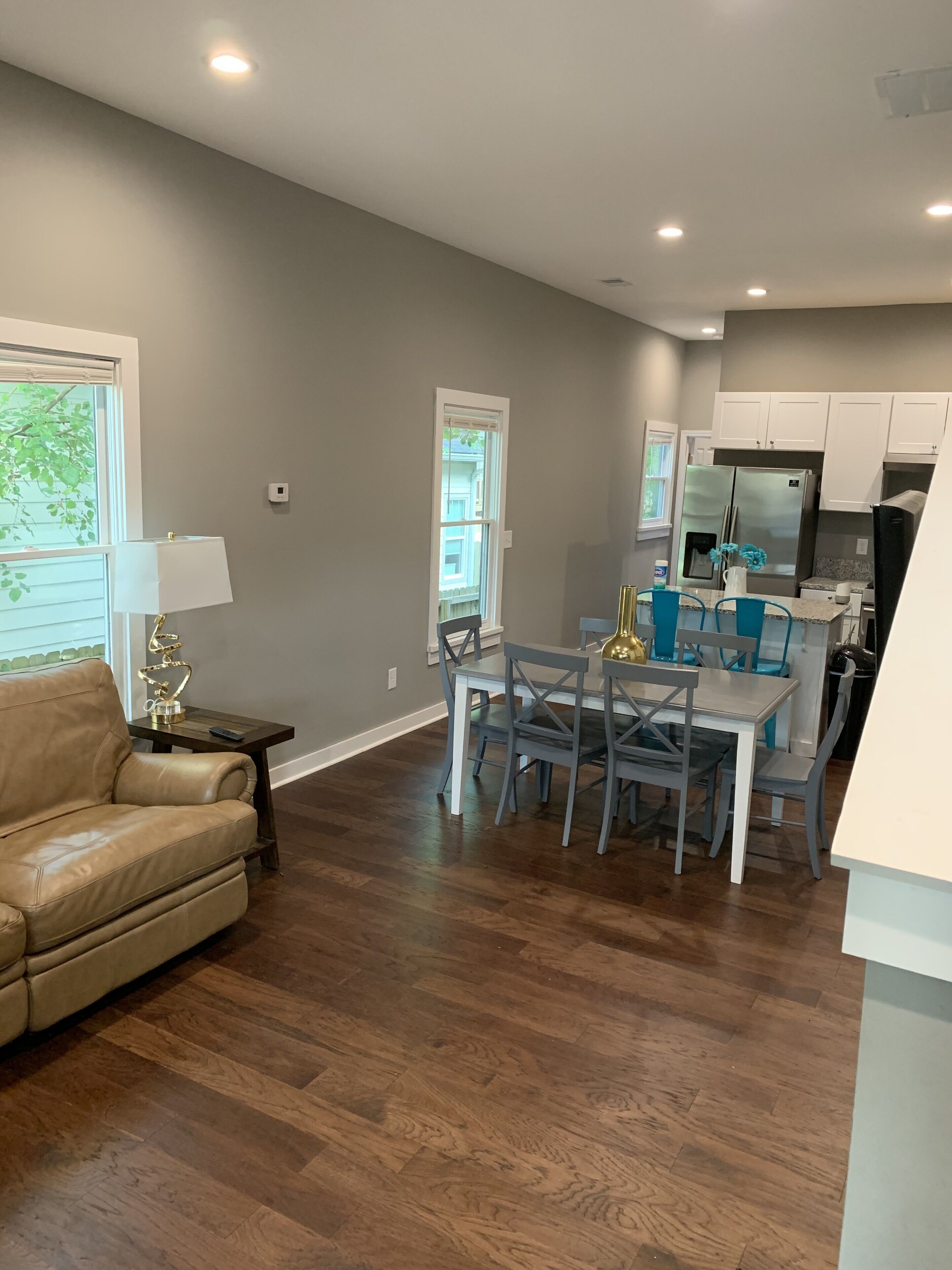 A spacious living room with a leather sofa, a dining area with a table and chairs, and a kitchen with white cabinets and stainless steel appliances.