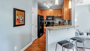 Una cocina moderna con armarios de madera, un refrigerador negro, un microondas y una encimera de granito. Hay dos taburetes de bar y un cuadro en la pared.