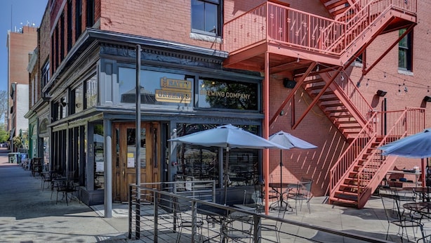 Un edificio de ladrillo con un letrero que dice 'Natty's Brewing Company' y asientos al aire libre con sombrillas.