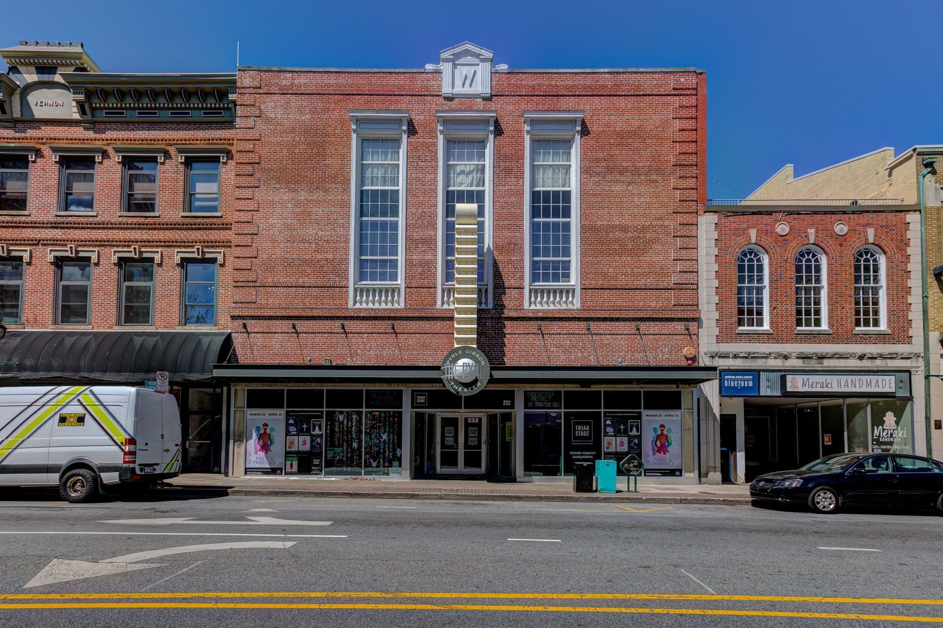 A brick building with a theater entrance, a van, and a car parked in front.