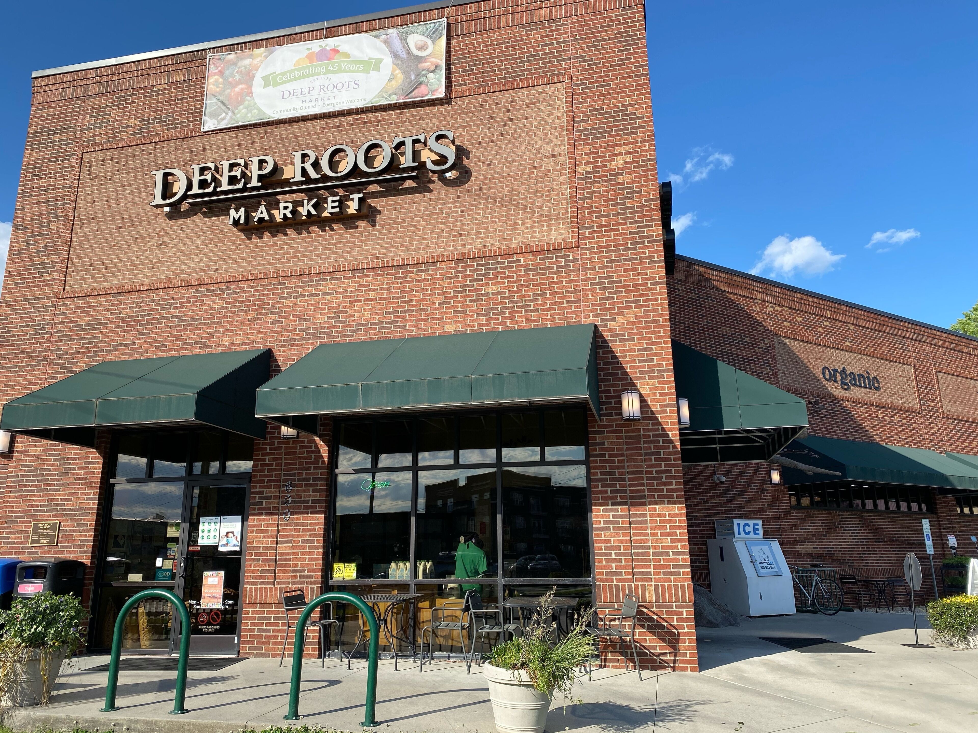 The exterior of Deep Roots Market with a brick facade, green awnings, and outdoor seating area.