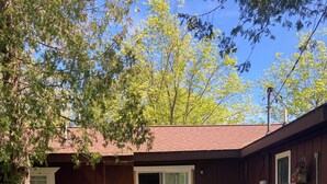 A wooden deck with outdoor furniture, a barbecue grill, and a covered patio area. - Lakeside condo. (Oscoda)
