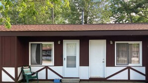 A single-story building with a brown and white exterior, a front door, and a window on the left side. - Lakeside condo. (Oscoda)