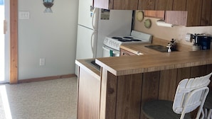 A kitchen with wooden cabinets, a white refrigerator, a stove, and a bar area with two stools. - Lakeside condo. (Oscoda)