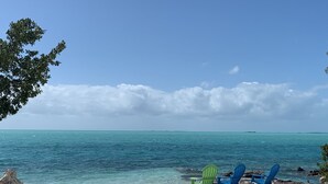 A beach with clear turquoise water, a sandy shore, and two green and blue Adirondack chairs.