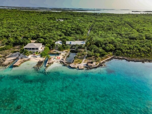 An aerial view of a coastal property with multiple buildings, clear turquoise waters, and dense greenery.