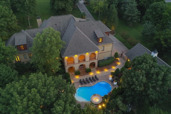 Vista aérea de una casa grande con piscina, rodeada de árboles y un césped bien cuidado.