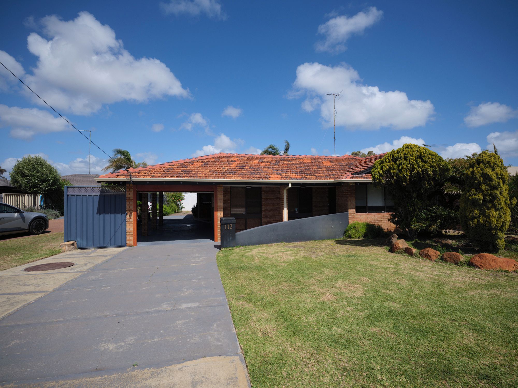 A residential house with a red-tiled roof, a covered porch, and a front yard with grass and rocks.