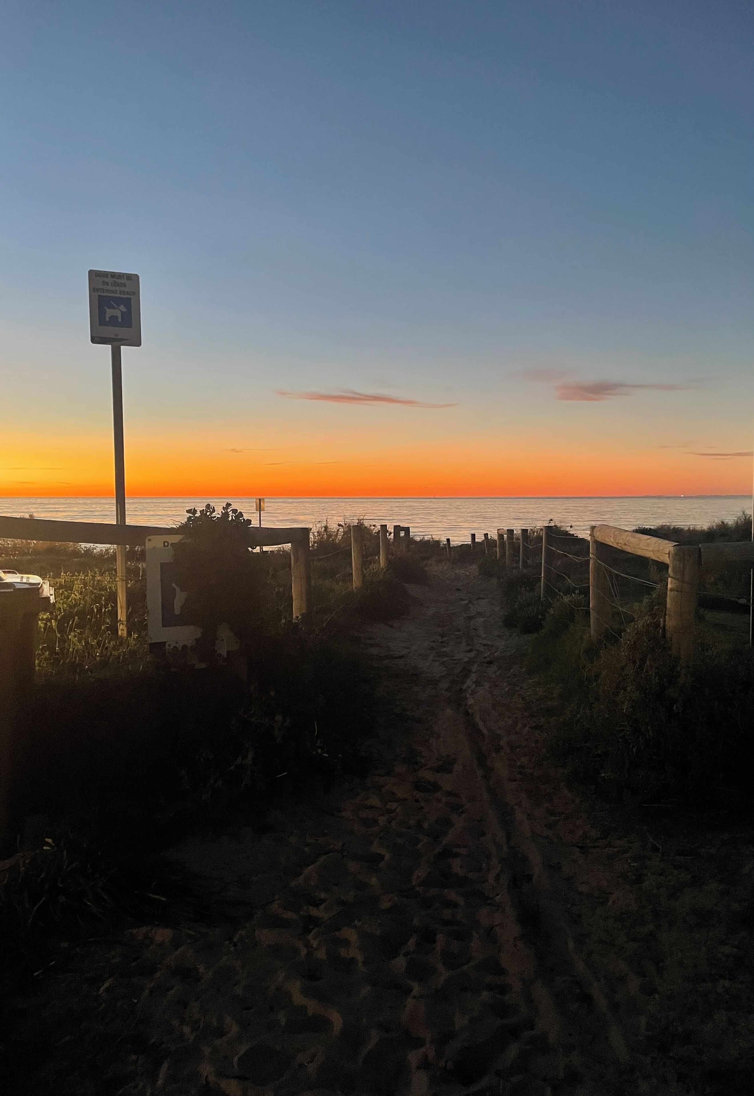 A beach path leading to the sea with a sign indicating a dog must be on a leash.
