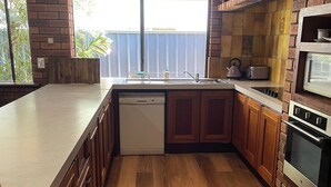 A kitchen with wooden cabinets, a dishwasher, a microwave, and a window with a view of greenery. - Town Beach Short Stay on Ormsby Terrace                   Beach across the Road. (Mandurah)