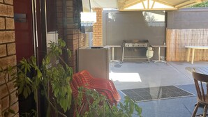 An outdoor patio area with a brick wall, a sliding glass door, a grill, and a seating area with a table and chairs. - Town Beach Short Stay on Ormsby Terrace                   Beach across the Road. (Mandurah)