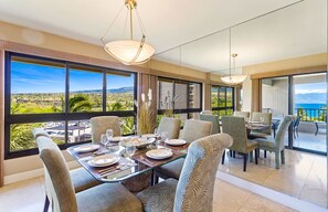 Un coin repas avec une table dressée pour quatre personnes, de grandes fenêtres offrant une vue sur le paysage et un balcon avec vue sur la mer.