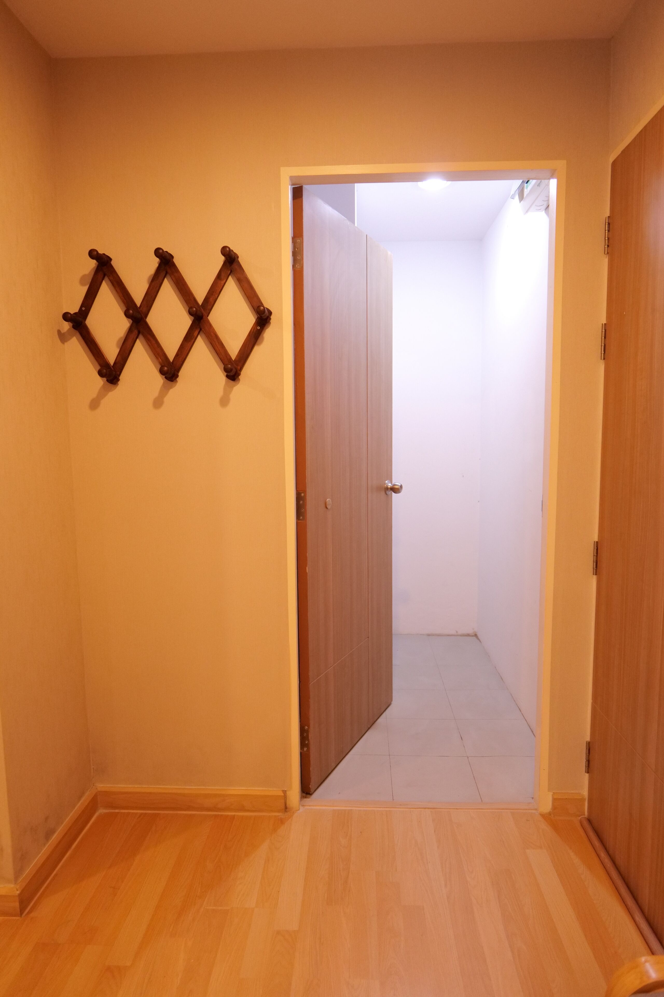 A hallway with wooden flooring, a wooden door, and a wall-mounted wooden rack.