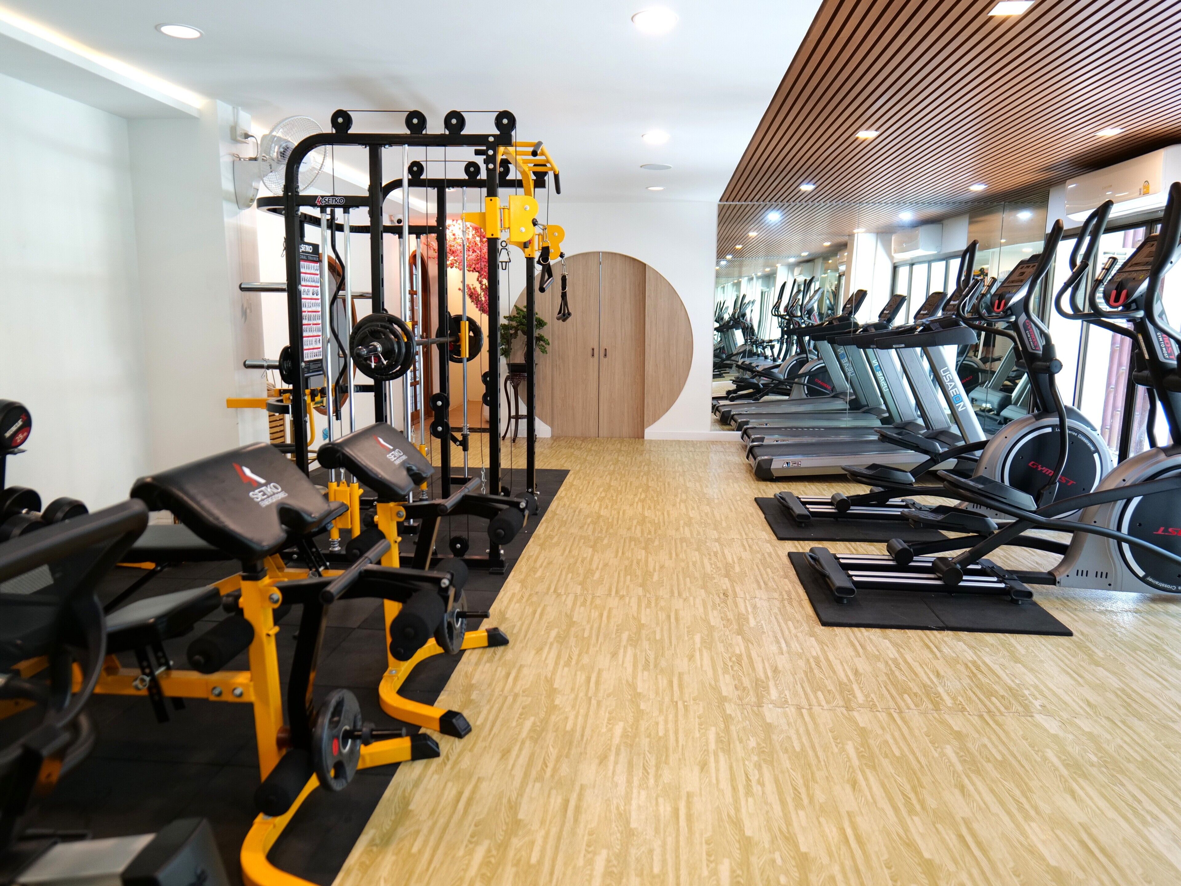 A gym with exercise equipment, treadmills, and a wooden floor.