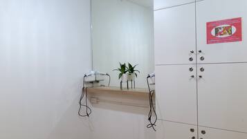 Una habitación con un espejo, una estantería con una planta y un armario con cerraduras numeradas.