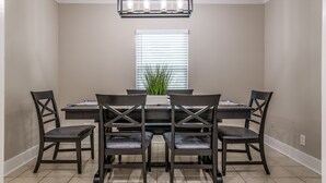 A dining room with a rectangular table, six chairs, a chandelier, a potted plant, and a window with blinds. - Charming entire house only 5 miles from Truist Park. (Smyrna)