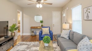 A living room with a ceiling fan, a sofa, a coffee table, and a TV. - Charming entire house only 5 miles from Truist Park. (Smyrna)