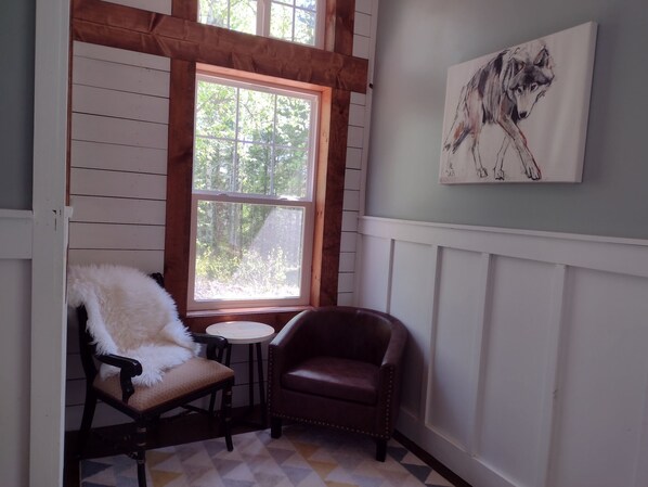 A cozy corner with a wooden chair and a leather armchair, a small round table, and a painting of a wolf on the wall. - Charming and Secluded North Shore Cabin and Sauna two miles from Grand Marais! (Grand Marais)