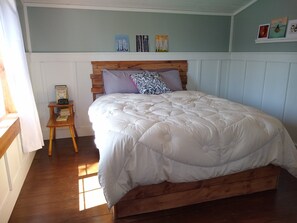 Ein Schlafzimmer mit einem hölzernen Bettgestell, einer weißen Bettdecke und einem kleinen Nachttisch mit Uhr und Büchern.