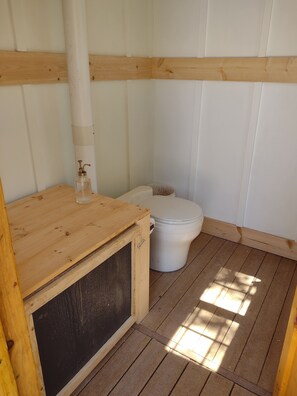 Ein kleines, kompaktes Badezimmer mit Holzboden, Toilette in Weiß und einem Holzschrank mit Seifenspender.