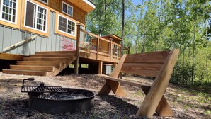 A wooden deck with a fire pit and a bench, surrounded by trees.