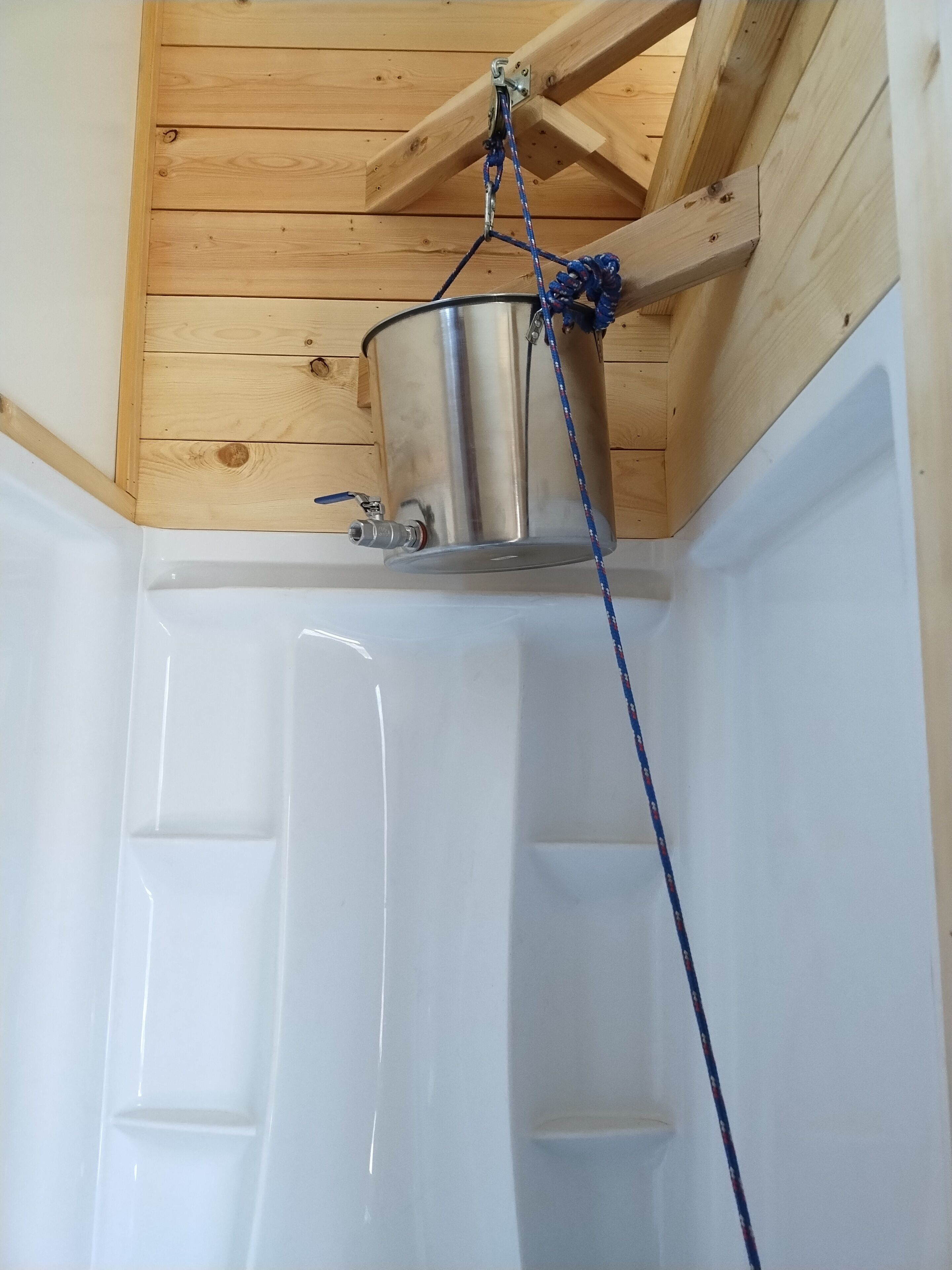 A corner of a room with a wooden ceiling, a white bathtub, and a metal container hanging from the ceiling.