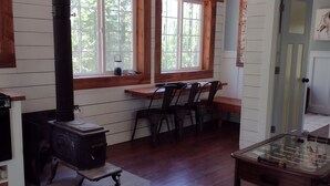A cozy room with a wood-burning stove, large windows, a foosball table, and a dining area with chairs.