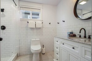 A bathroom with a toilet, a shower enclosure, a vanity with a sink, and a mirror. - Mid-City NOLA Getaway, Great for Groups! (New Orleans)