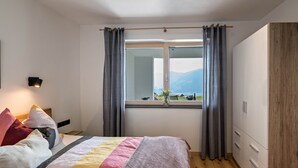 Ein Schlafzimmer mit Bett, Vorhängen am Fenster, einem Nachttisch und einer Wandlampe.