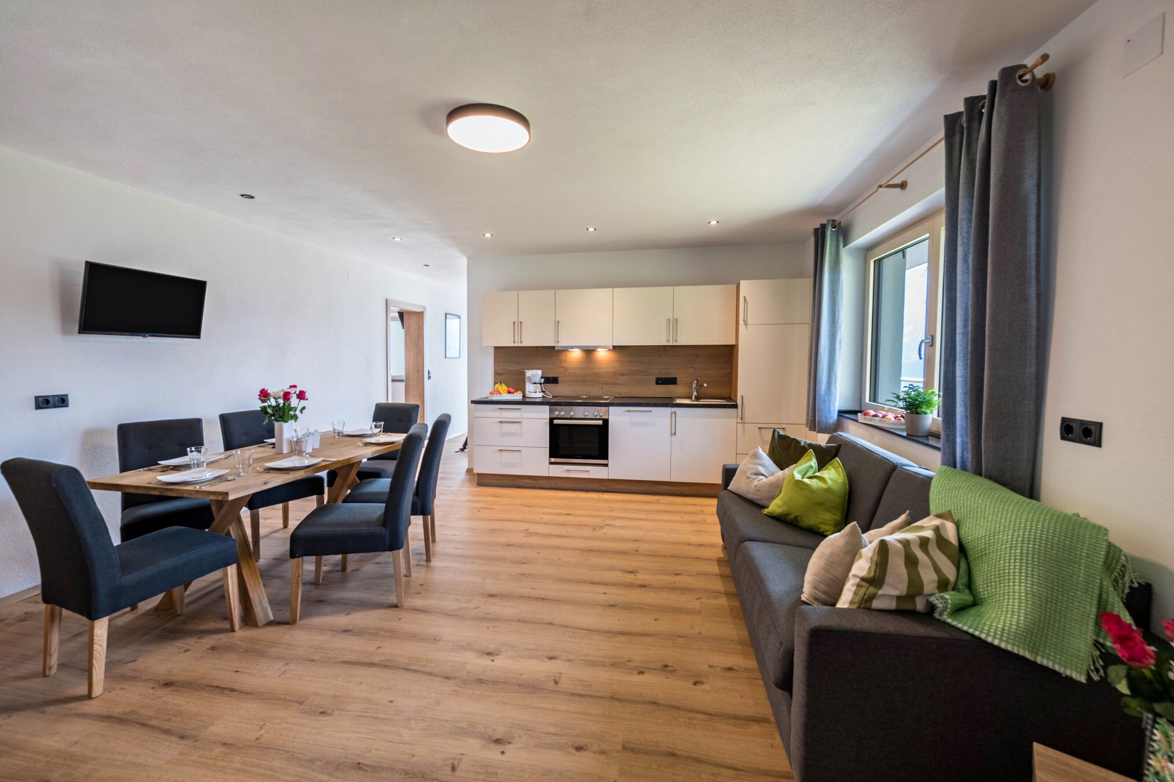 Een moderne woonkamer met een eethoek, keuken en een groot raam met gordijnen.