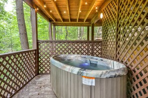 Un bain à remous sur une terrasse en bois, entouré d’une clôture en treillis et bordé d’arbres.
