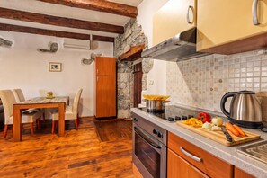 Una cuina amb armaris de fusta, paret de pedra, salabost i zona de menjador amb taula i cadires.