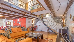 A spacious living area with a high ceiling, wooden beams, a staircase, and a red accent wall.