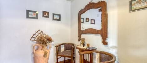 A corner with a large vase, two wooden chairs, a small table, and a mirror on the wall.
