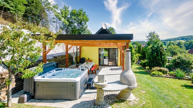Un bain à remous sous une pergola en bois, une fontaine en pierre et une vue sur un jardin luxuriant.