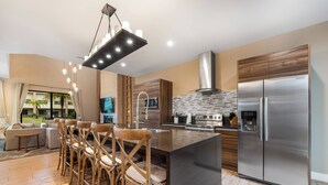 A modern kitchen with a stainless steel refrigerator, wooden chairs, and a large island. - 7458 Modern new home 3 suites jacuzzi 8 min Disney (Kissimmee)