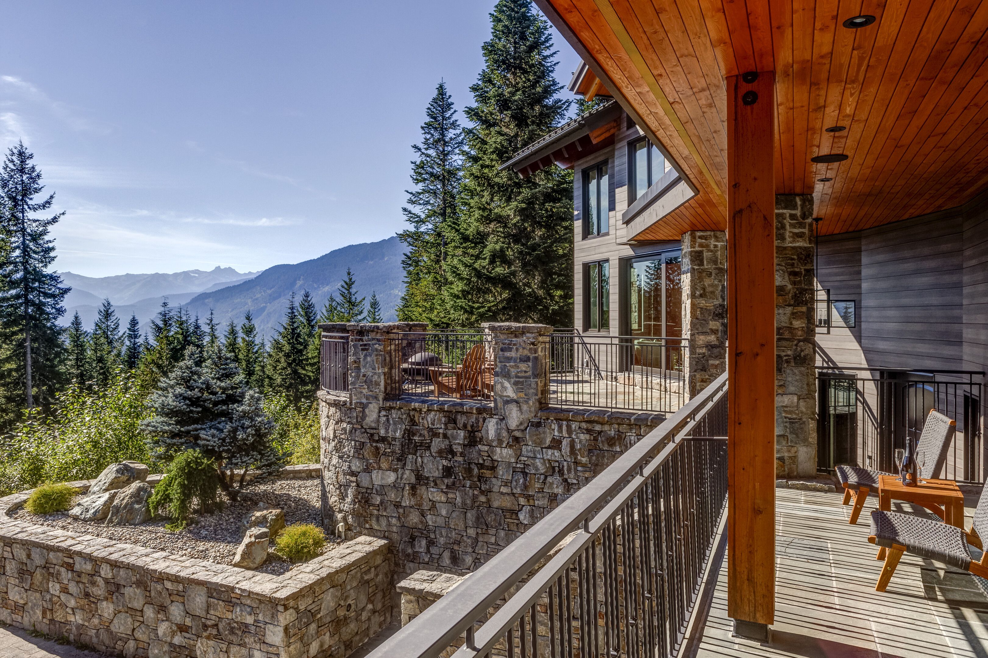 A modern building with a stone retaining wall, wooden deck, and outdoor seating area with a view of mountains.