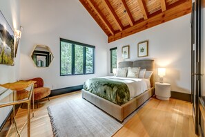 Ein Schlafzimmer mit einem großen Bett, einem Schreibtisch, einem Stuhl und einem Fenster mit Blick auf Bäume.