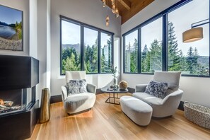 Ein modernes Wohnzimmer mit großen Fenstern, einem Kamin und zwei Sesseln.