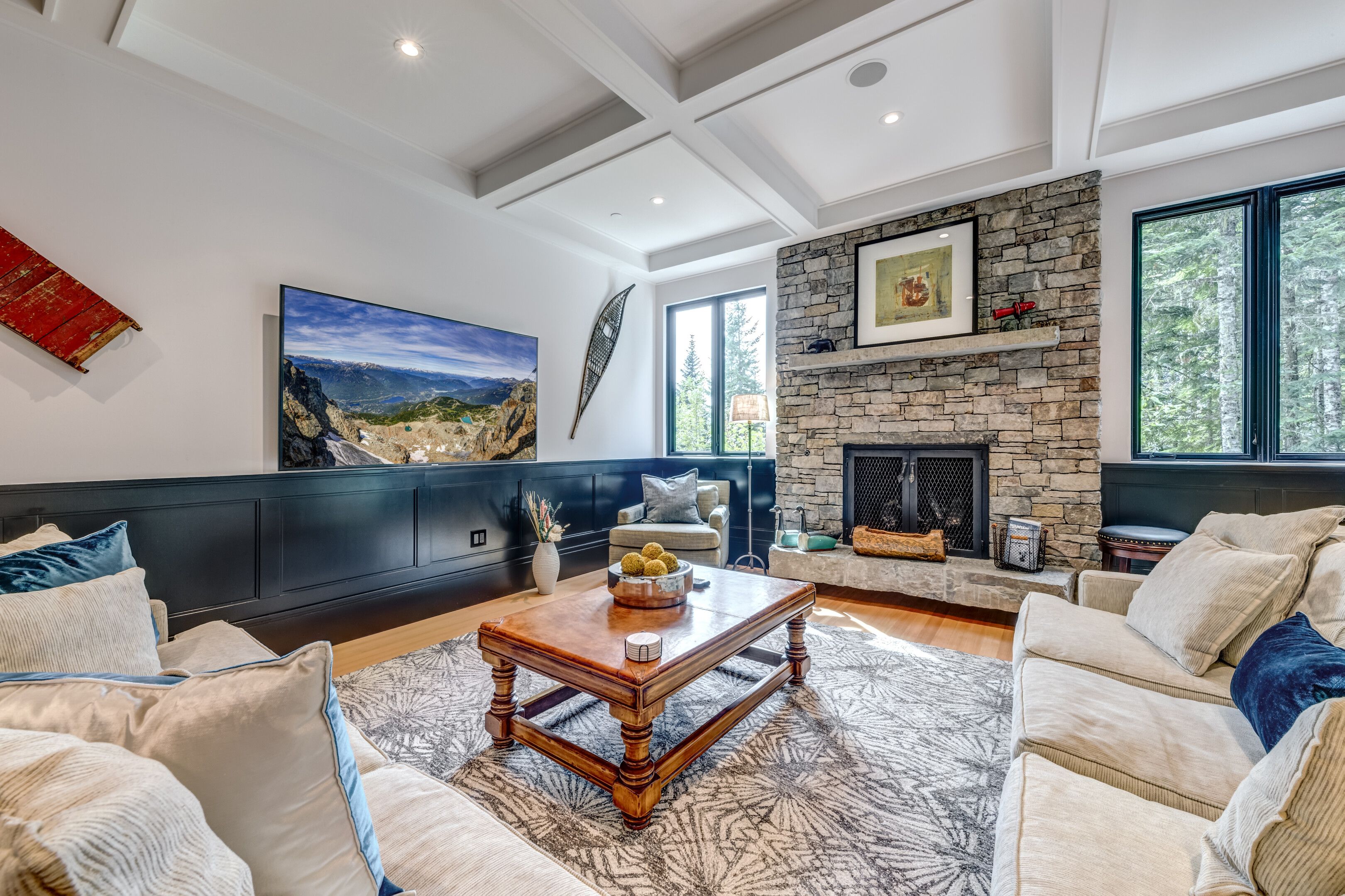 A modern living room with a stone fireplace, large windows, and a high ceiling.