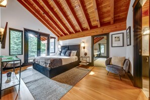 Ein modernes Schlafzimmer mit einem großen Bett, Holzbalkendecke, einem Glastisch und Blick ins Freie.