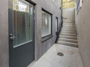 Una escalera estrecha que conduce a una puerta con ventana, barandilla metálica y pared de concreto.